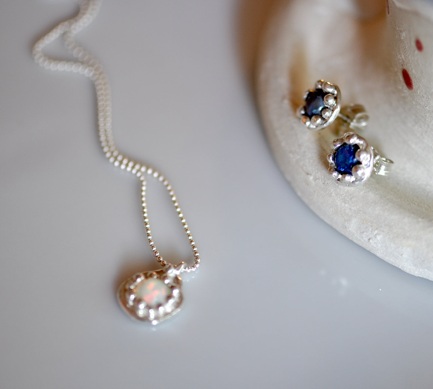 A silver opal necklace with a white and blue flower-shaped pendant and matching earrings, displayed on a white surface.