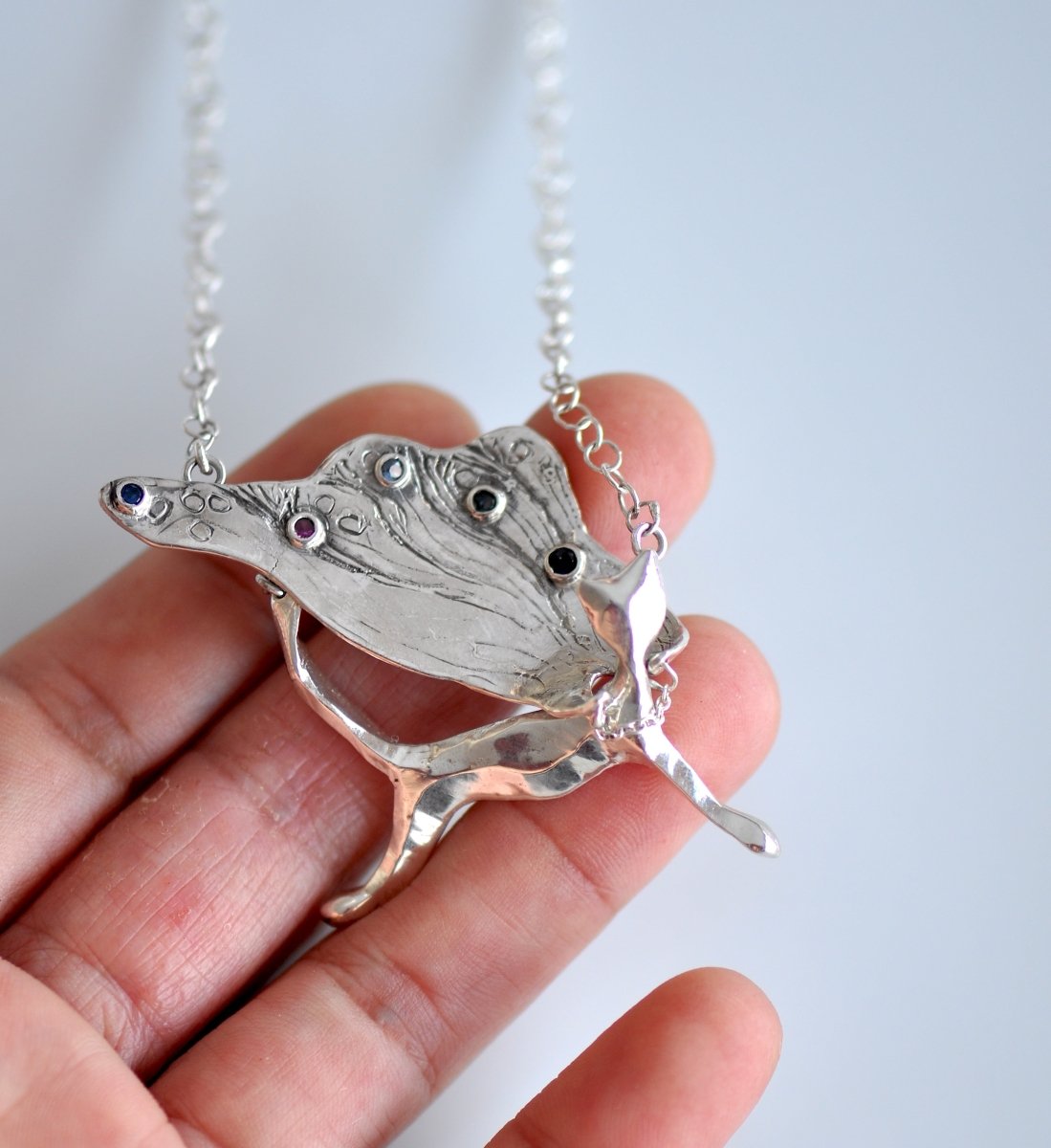 Handcrafted sterling silver necklace, whimsical cat pendant with a textured, wing-like cape, hanging on a silver chain.