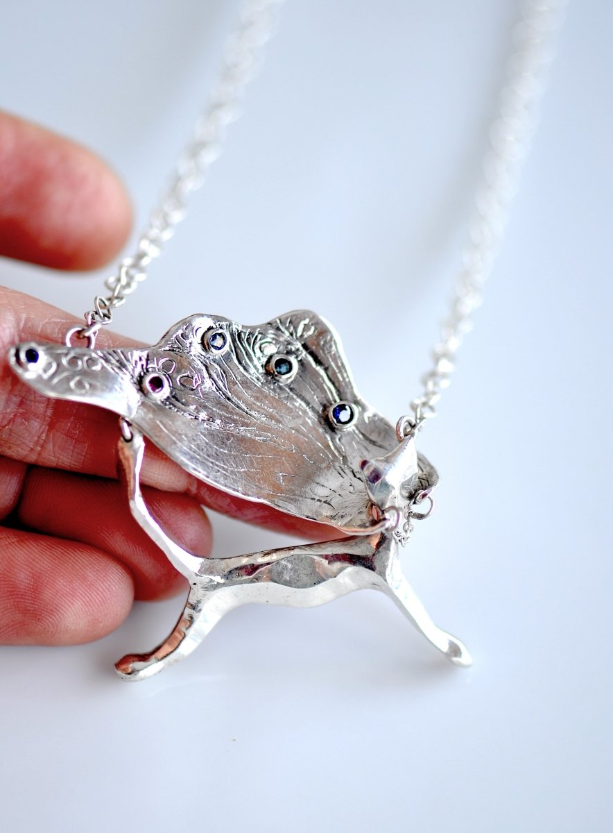 Handcrafted sterling silver necklace, whimsical cat pendant with a textured, wing-like cape, hanging on a silver chain.