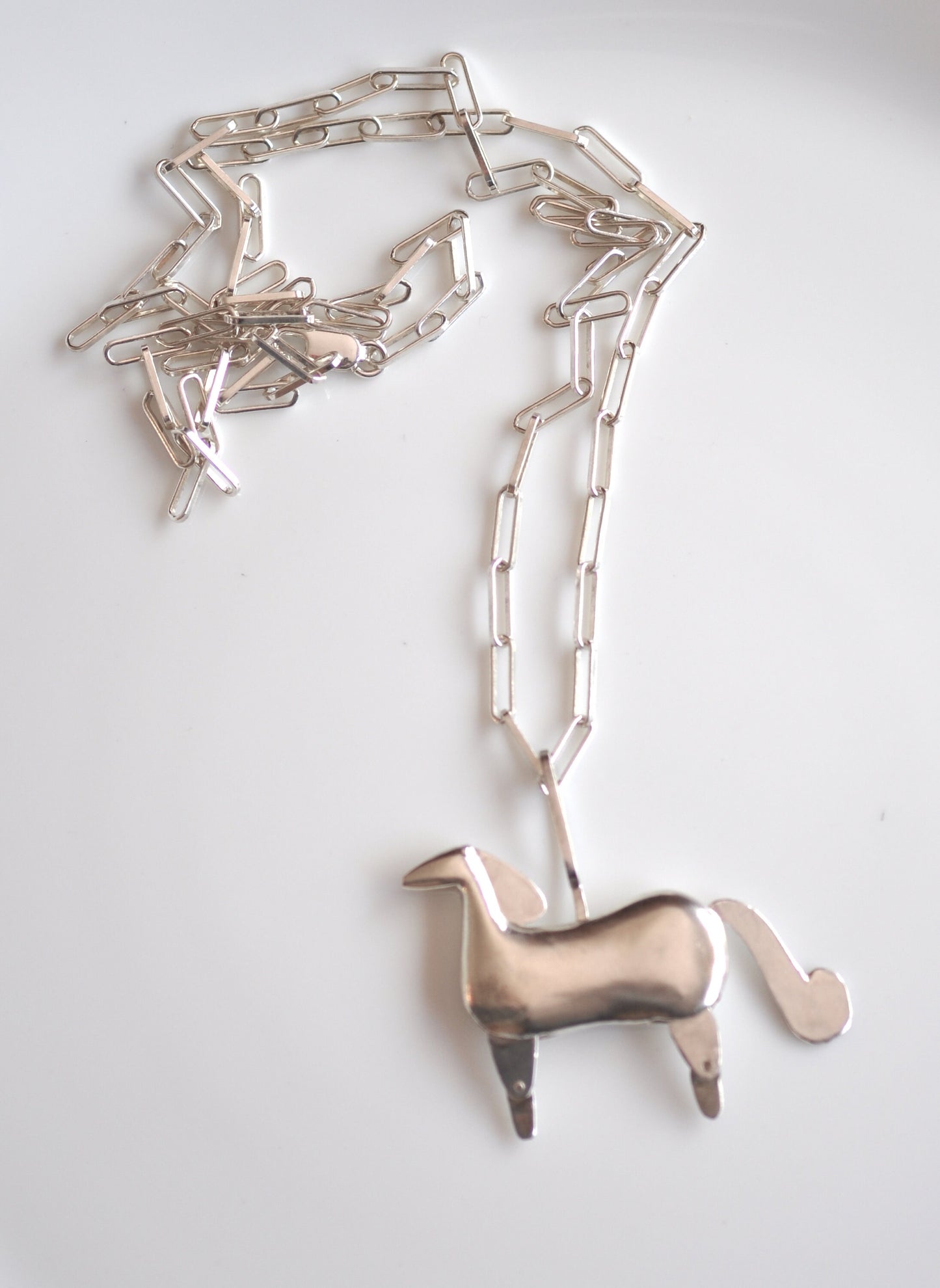 a metal horse on a chain on a white surface