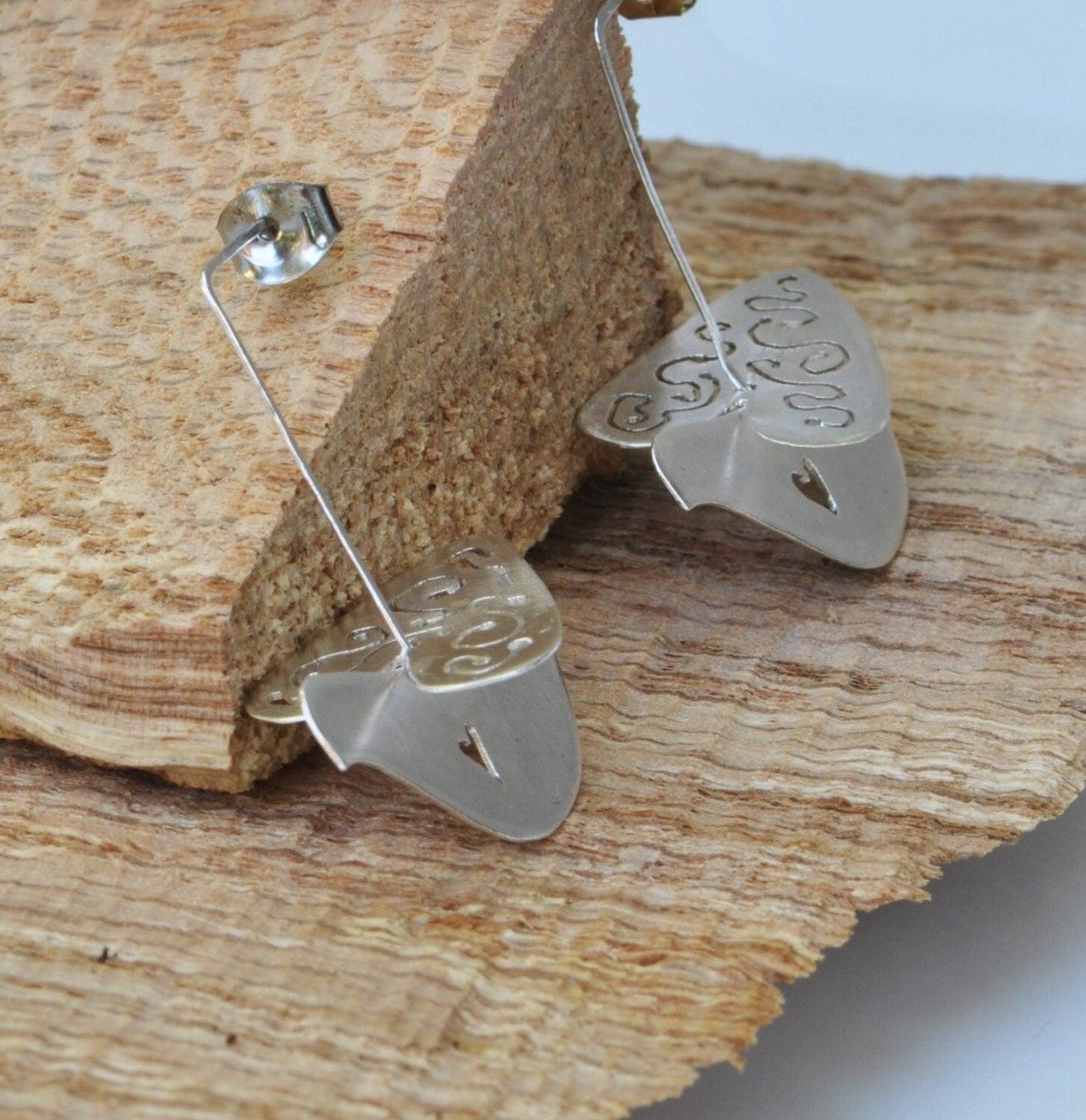 a pair of earrings sitting on top of a piece of wood