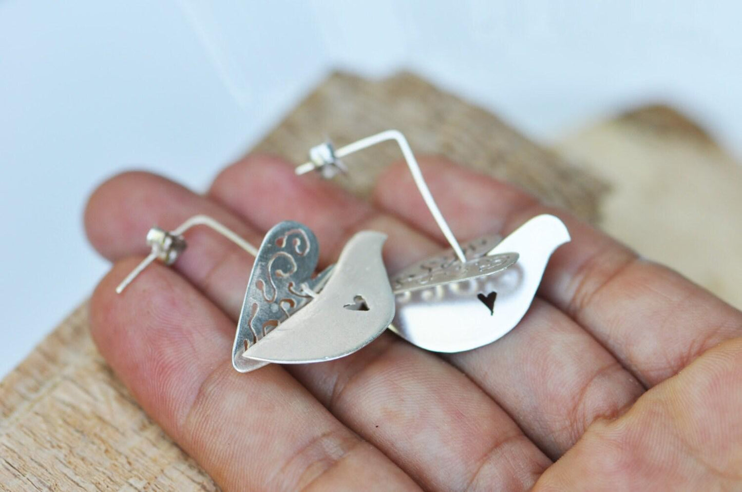 a pair of silver bird earrings on a person's hand