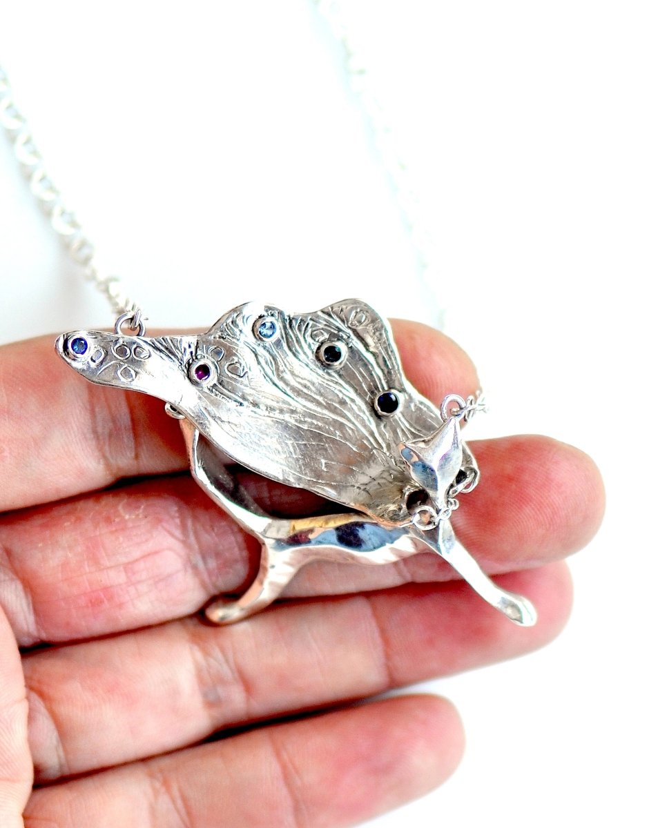 Handcrafted sterling silver necklace, whimsical cat pendant with a textured, wing-like cape, hanging on a silver chain.