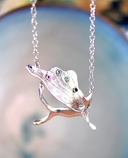 Handcrafted sterling silver necklace, whimsical cat pendant with a textured, wing-like cape, hanging on a silver chain.